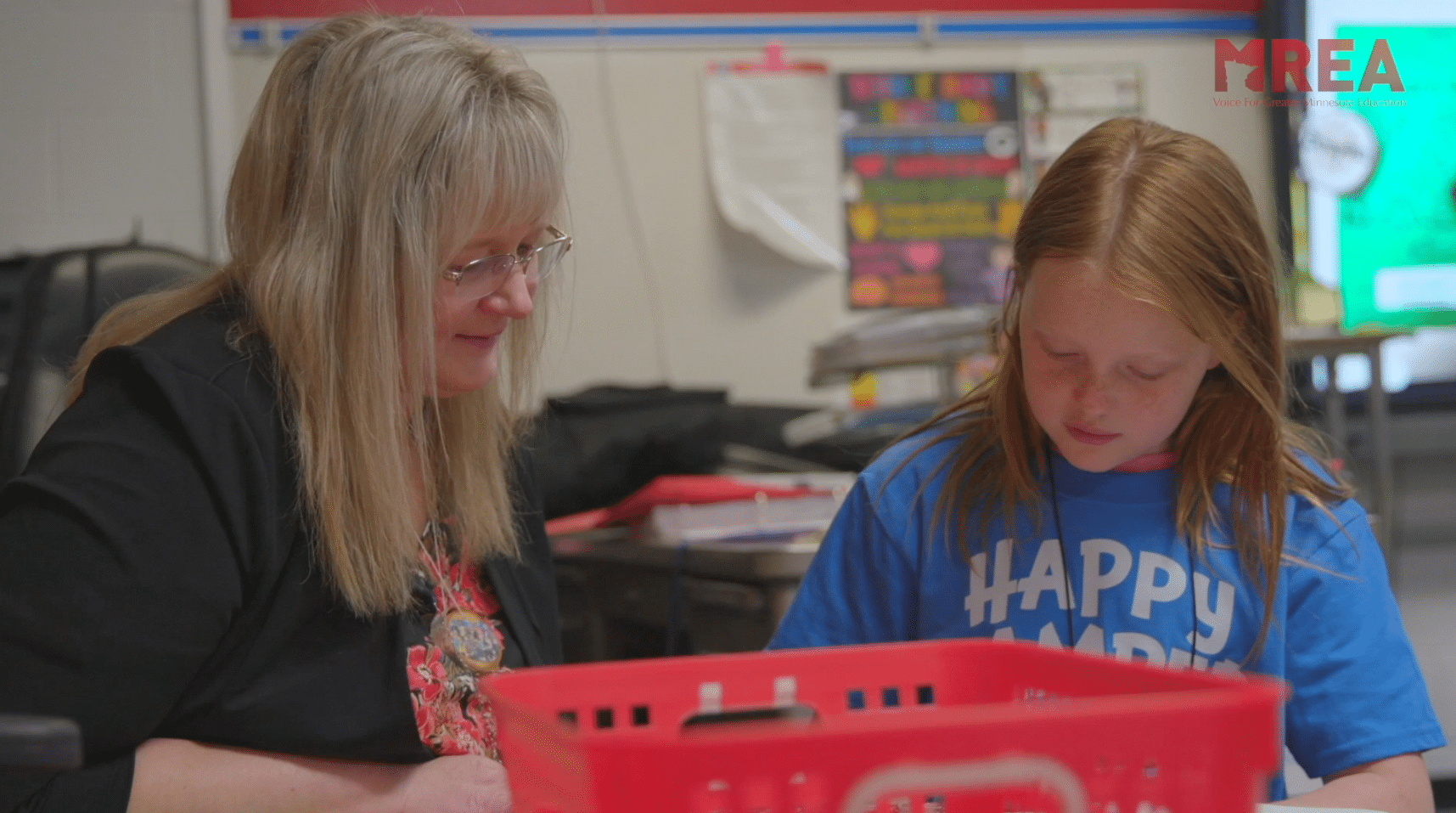 A teacher smiling and working with a student at a table.