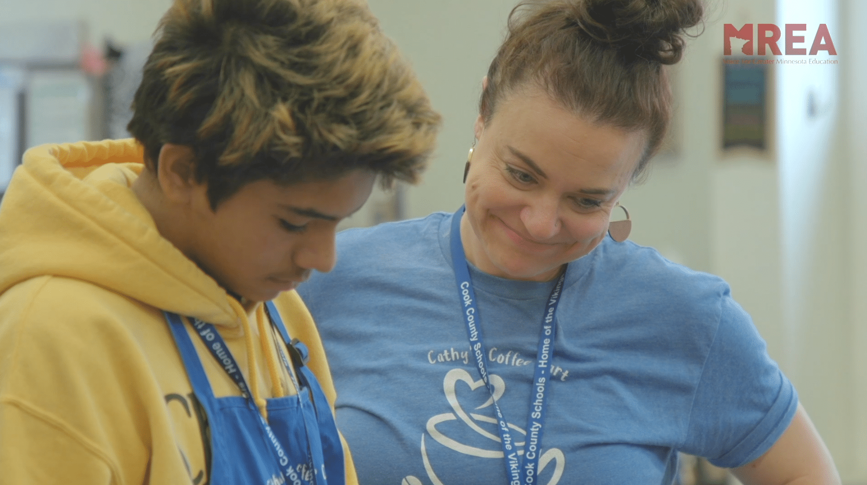 A teacher standing next to a student looking down at their work and smiling.