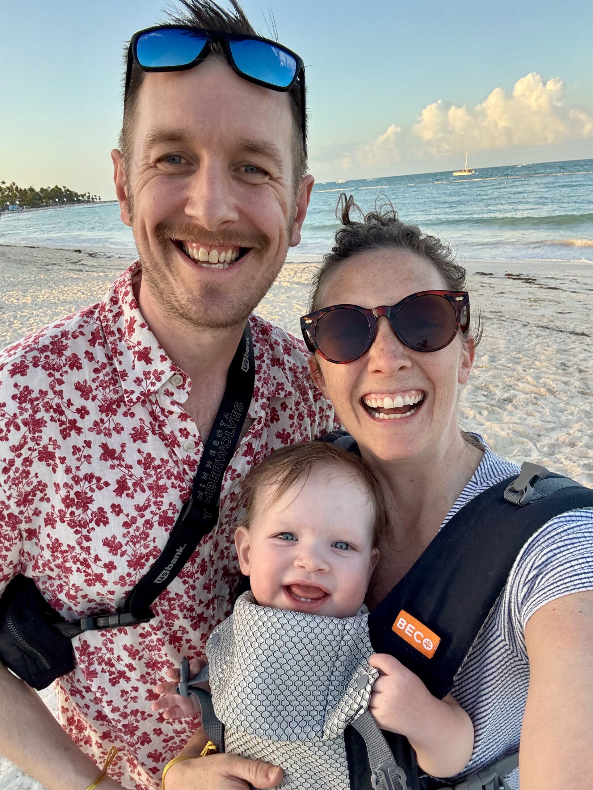 A man, a woman, and a baby smiling on the beach