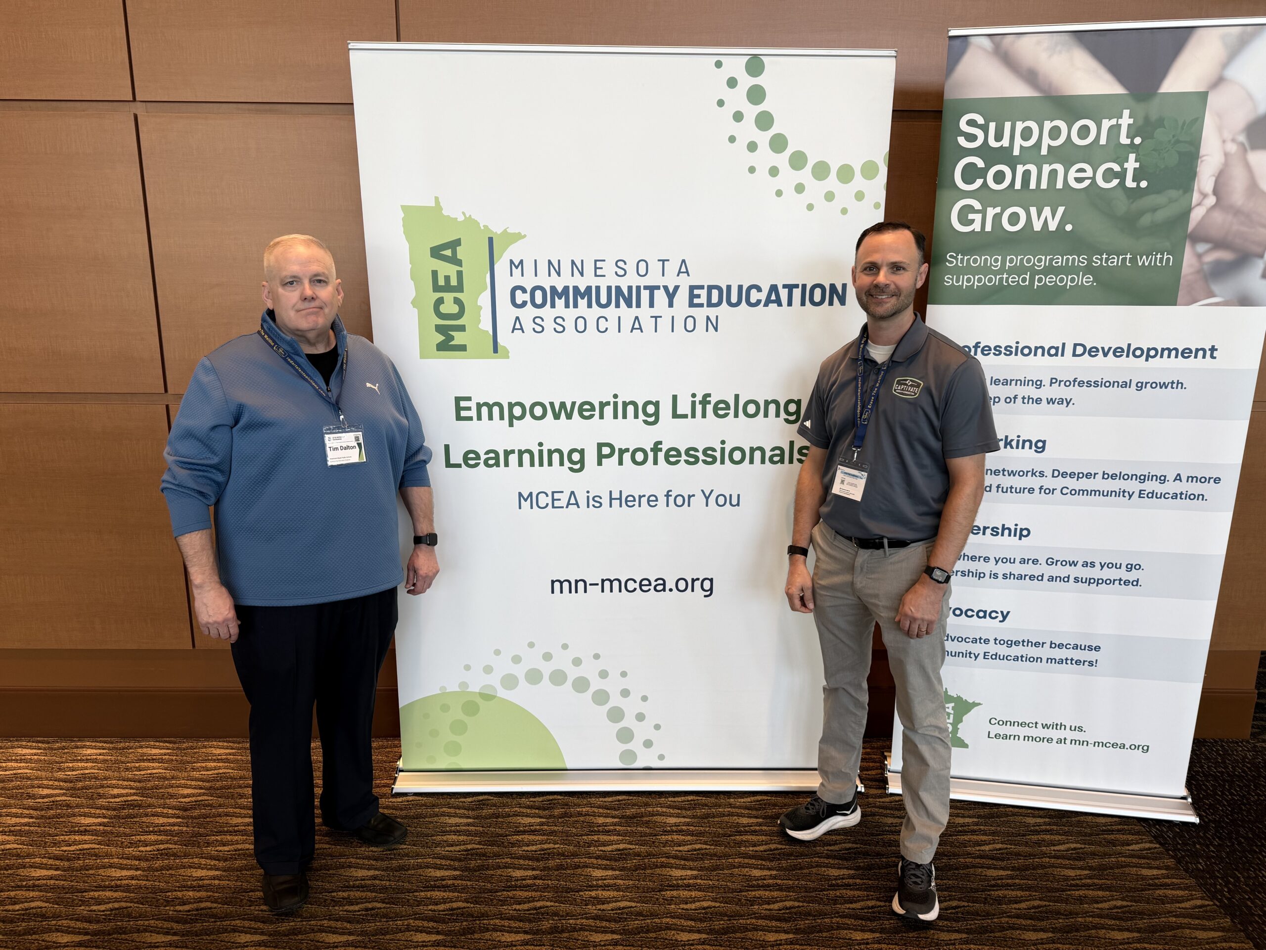 two men smiling on either side of a sign that reads "minnesota community education association"